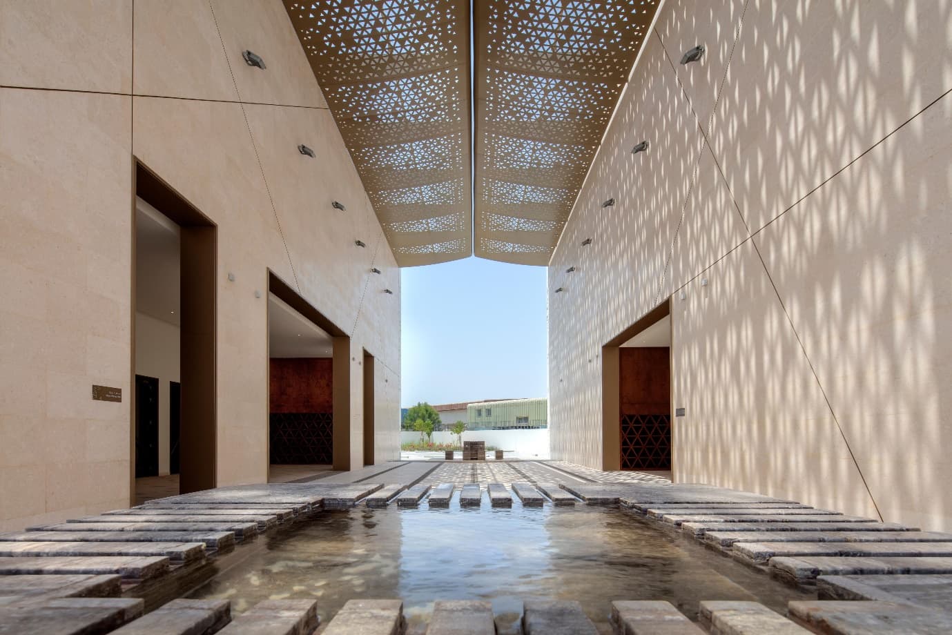A stone courtyard lit through a perforated geometric canopy